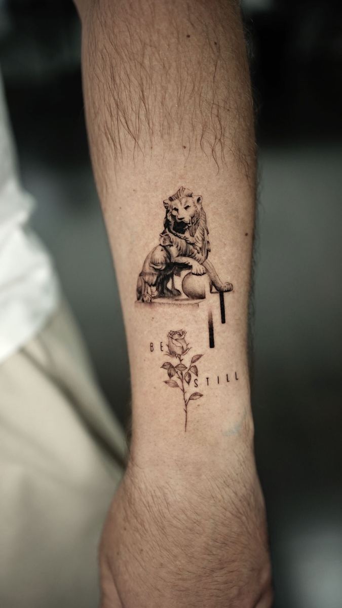 Black and gray lion tattoo with the text 'be still' and a rose.