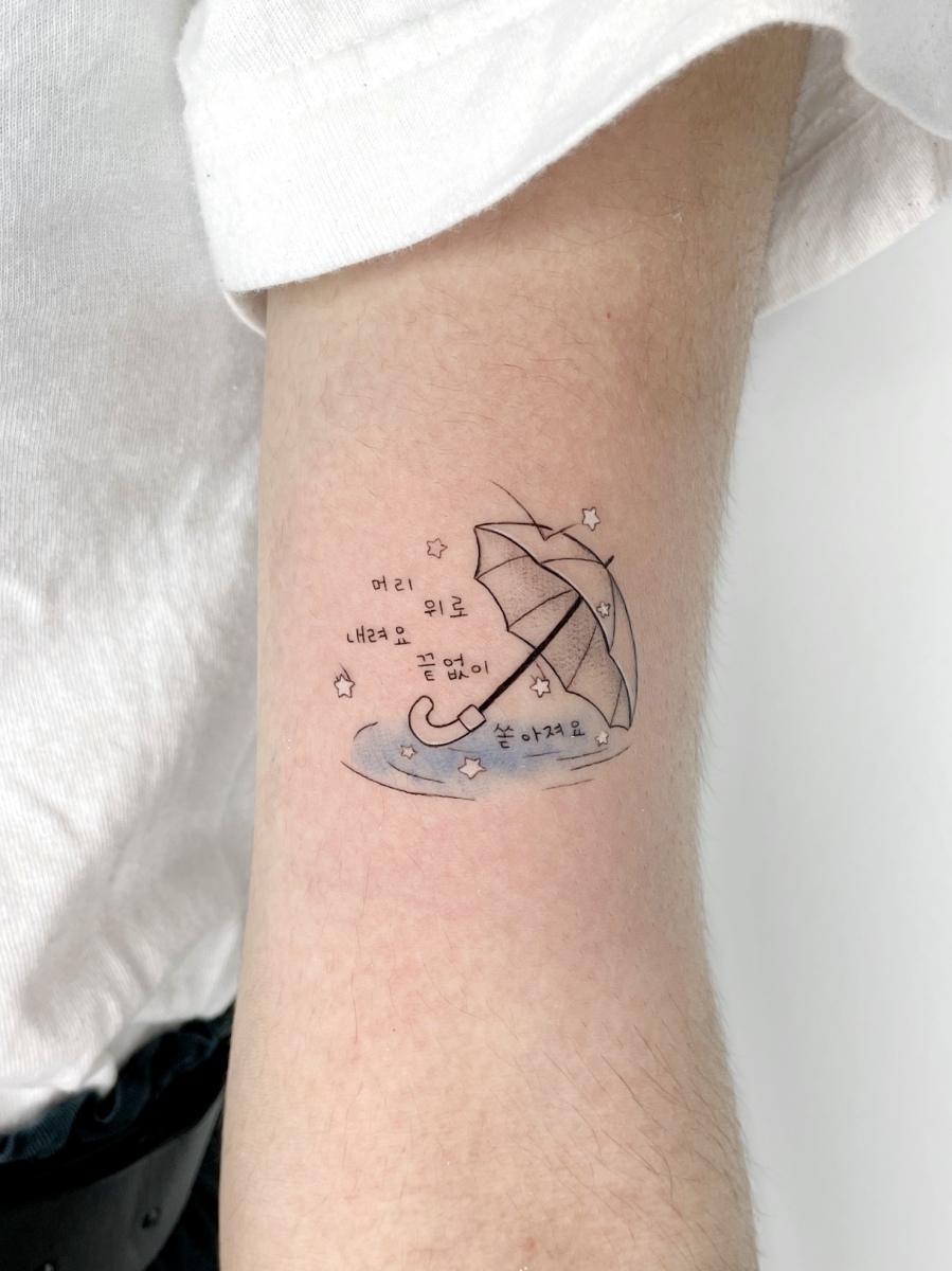 Black and gray tattoo of an umbrella and stars on a forearm