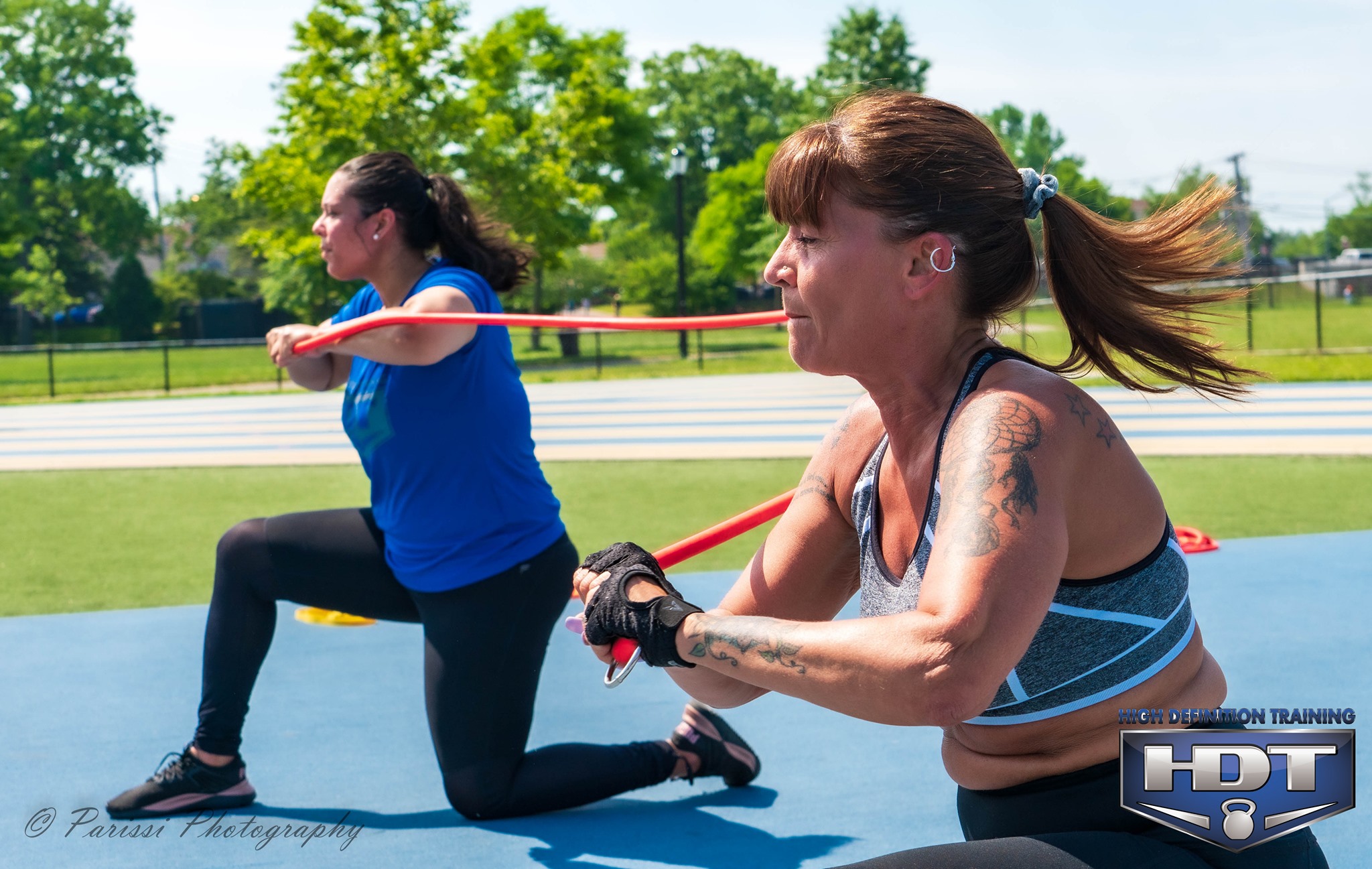 Two women performing resistance band exercises outdoors.