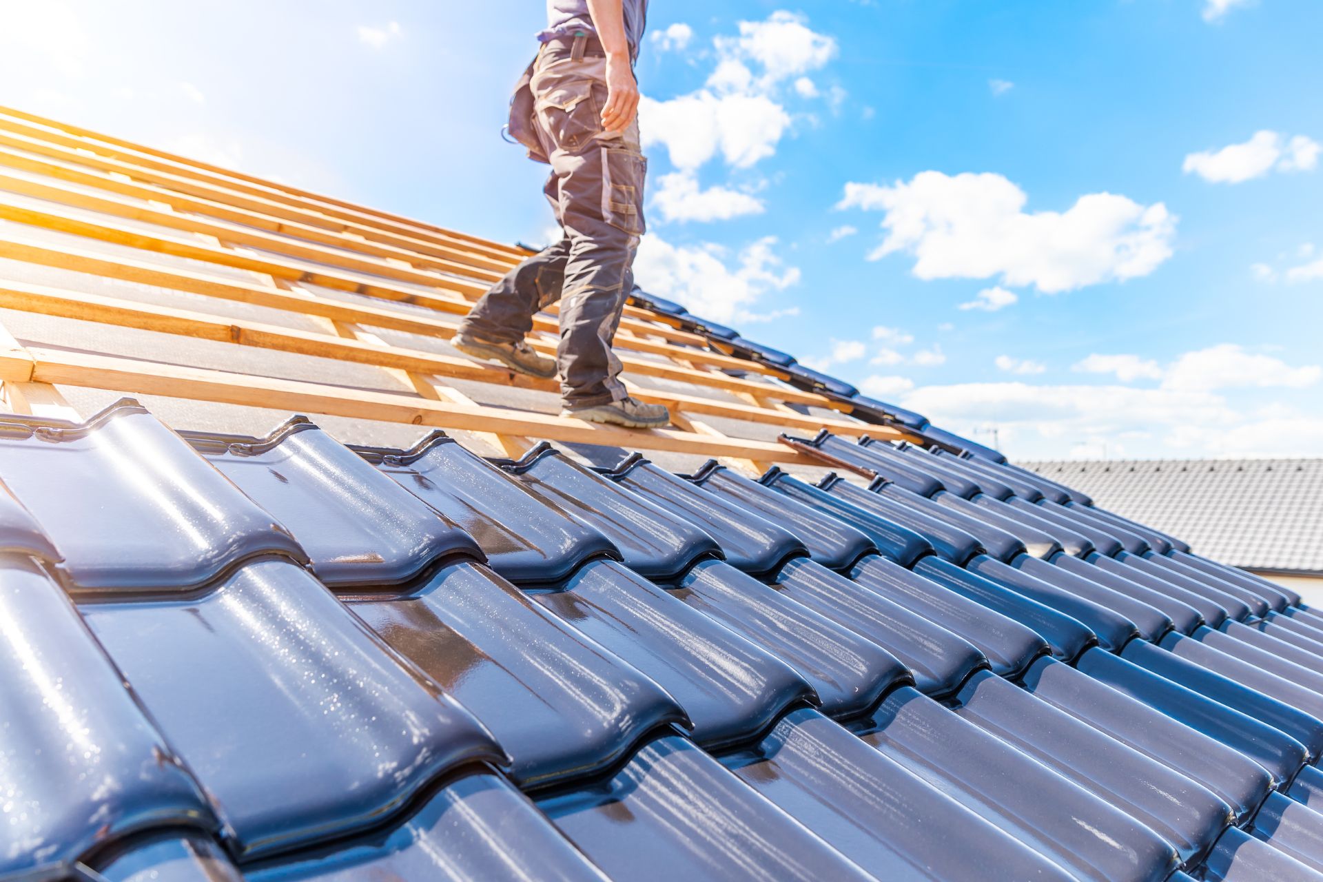 Roofer working on a blue tiled roof under a sunny sky.