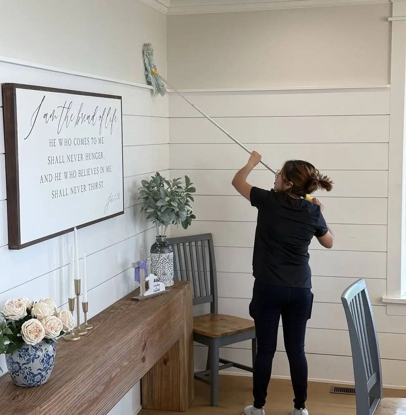 Person cleaning a wall with a mop in a bright room.