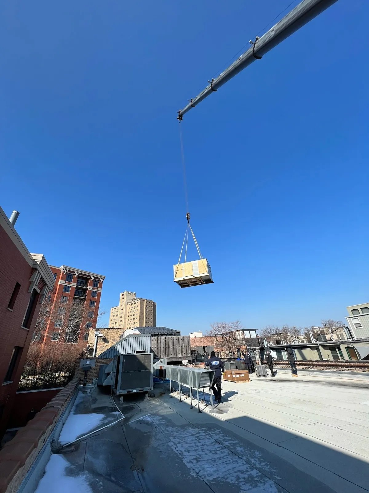 A crane lifting a large wooden crate against a blue sky.