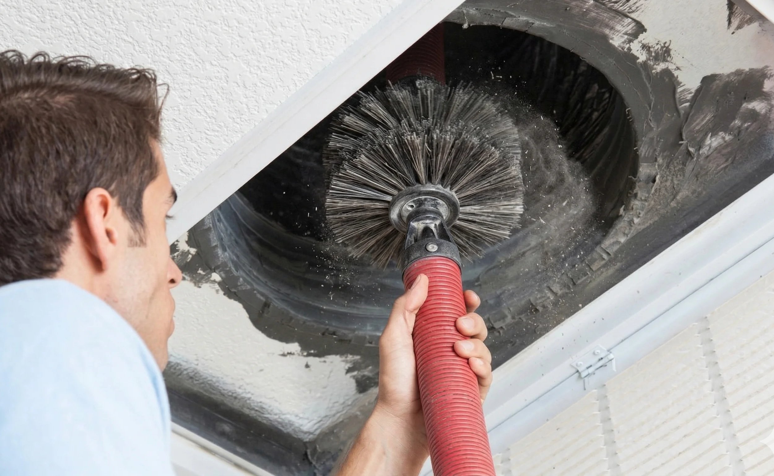 Person cleaning a ceiling duct with a brush and vacuum.