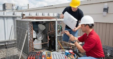 Technicians repairing an air conditioning unit on a rooftop.