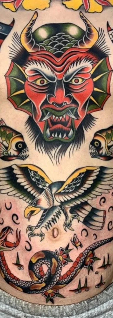 Vibrantly colored tattoo artwork on a man's torso featuring a devil face, fish, eagle, and snake.