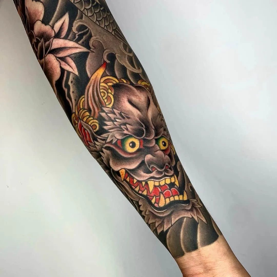 Tattoo of a fierce demon face on a forearm.