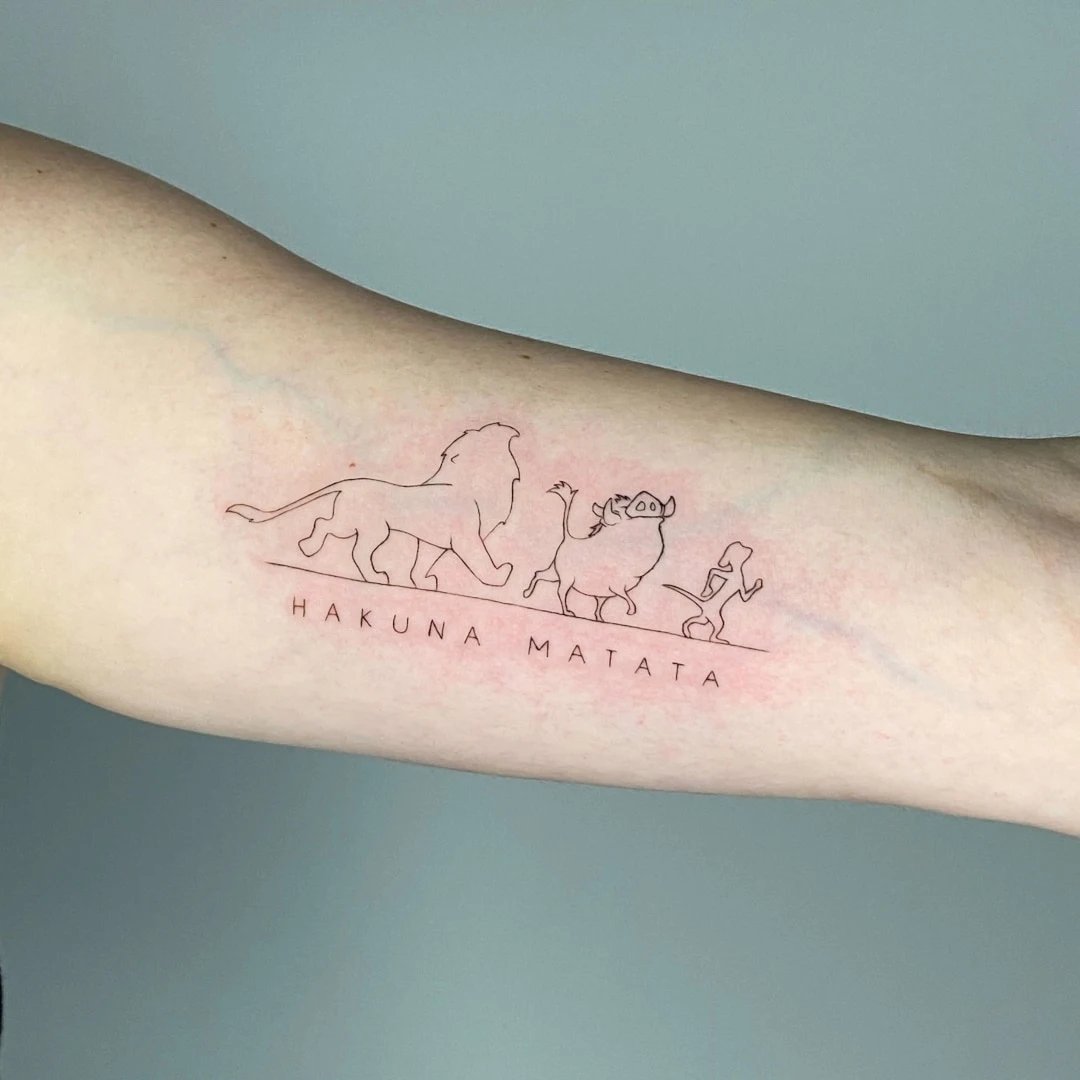 Tattoo featuring silhouette of lion, warthog, and meerkat with 'Hakuna Matata' text