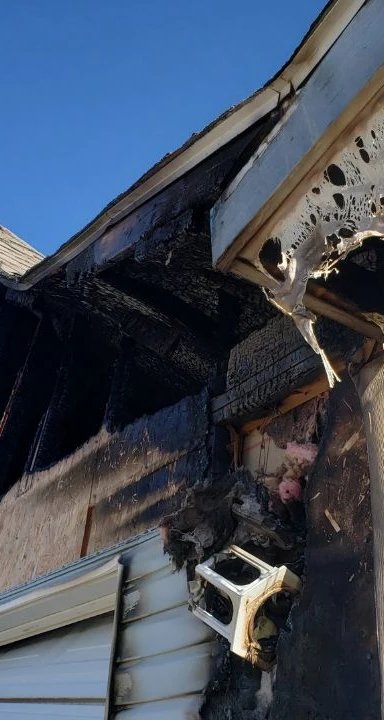 Severely burned residential building corner with exterior damage.