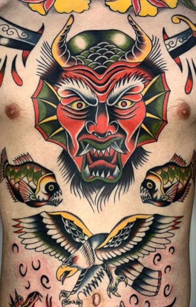 A person displaying a colorful tattoo design featuring a demon mask, fish, and an eagle on their torso.