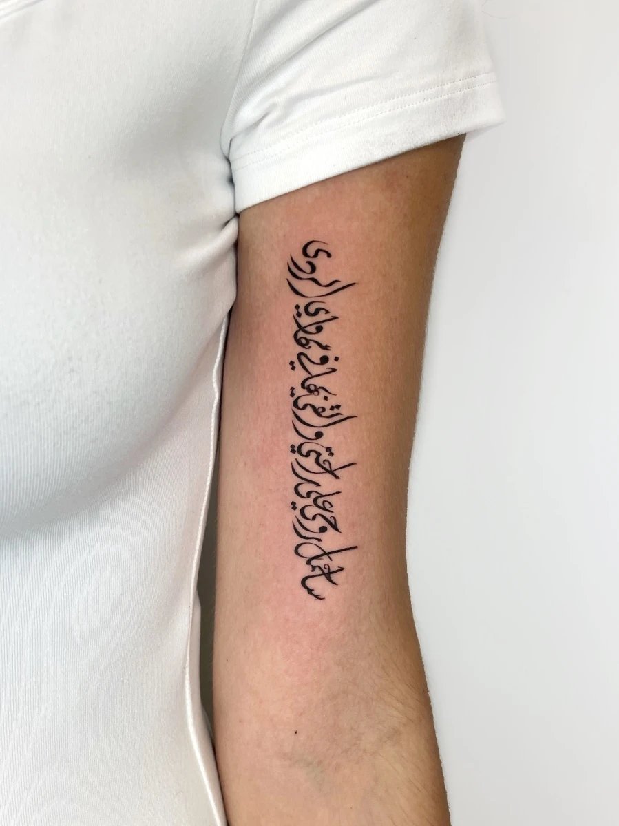 Close-up of a handwritten calligraphy tattoo on a forearm