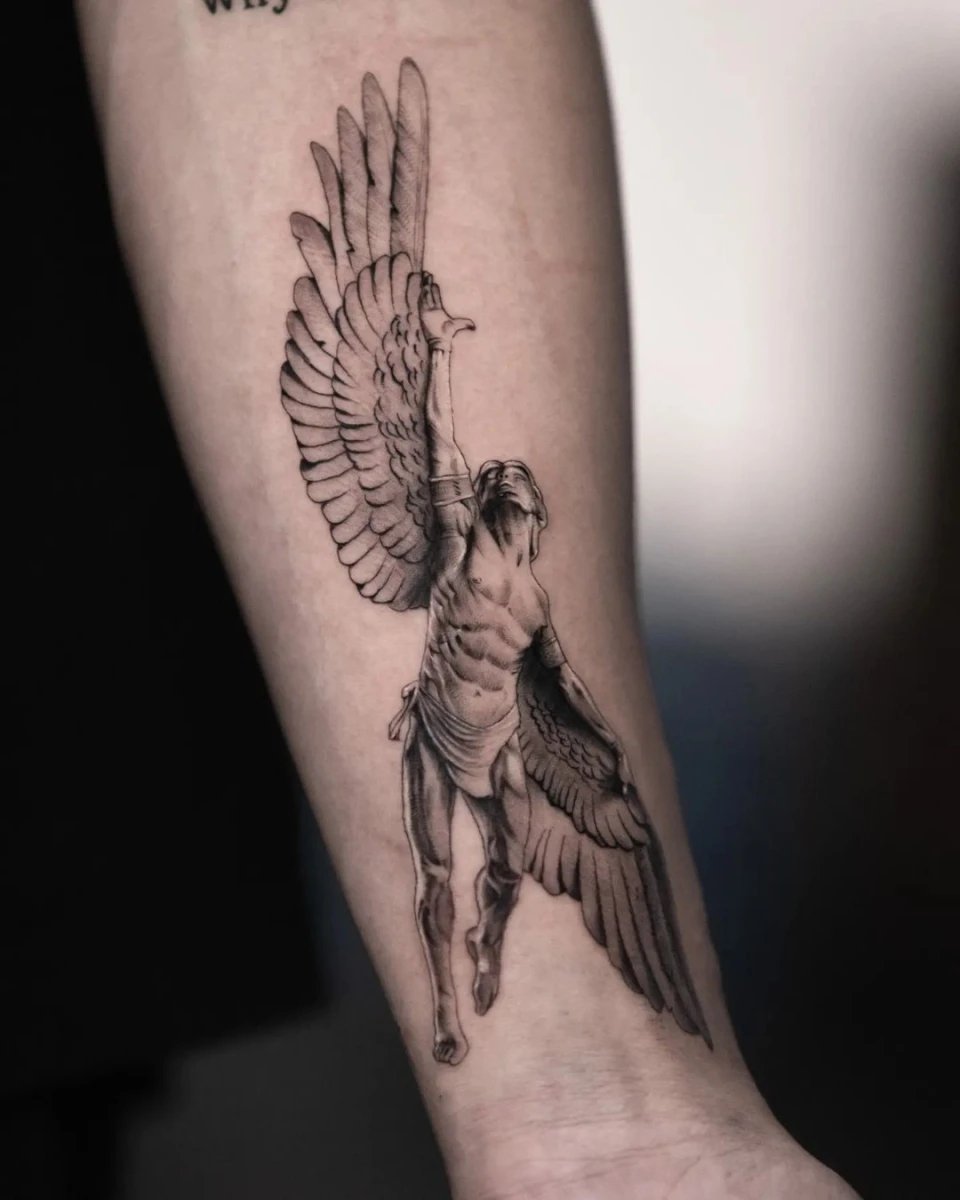 A detailed angel tattoo on a forearm, featuring wings and a muscular figure.