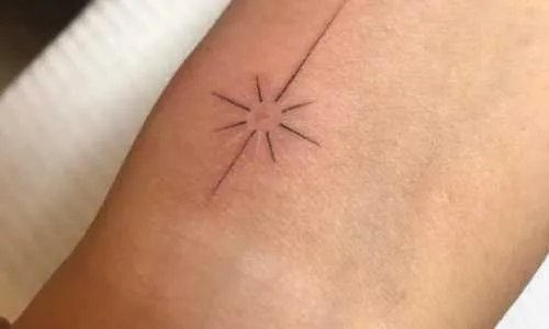 Minimalist tattoo of a starburst on skin.