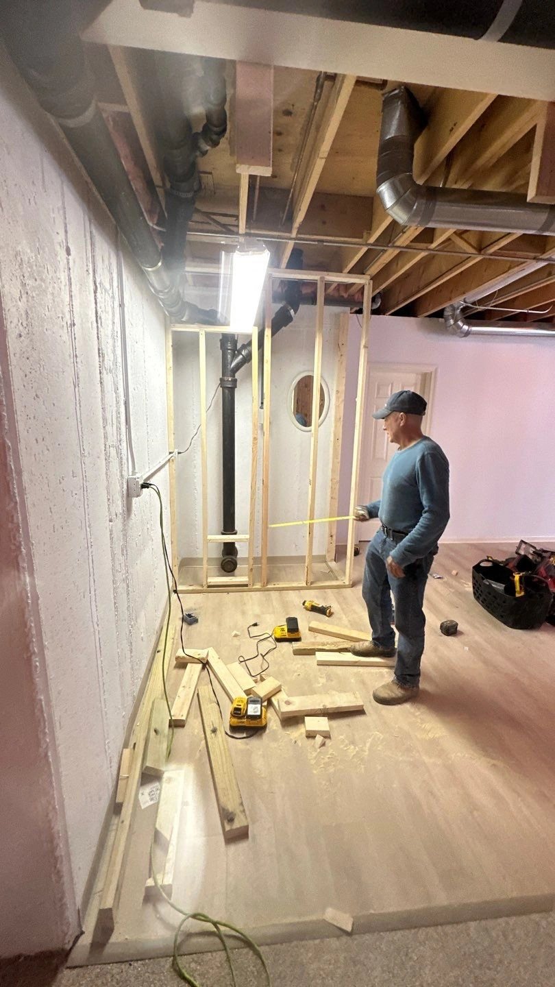 A man measures lumber in a basement construction site.