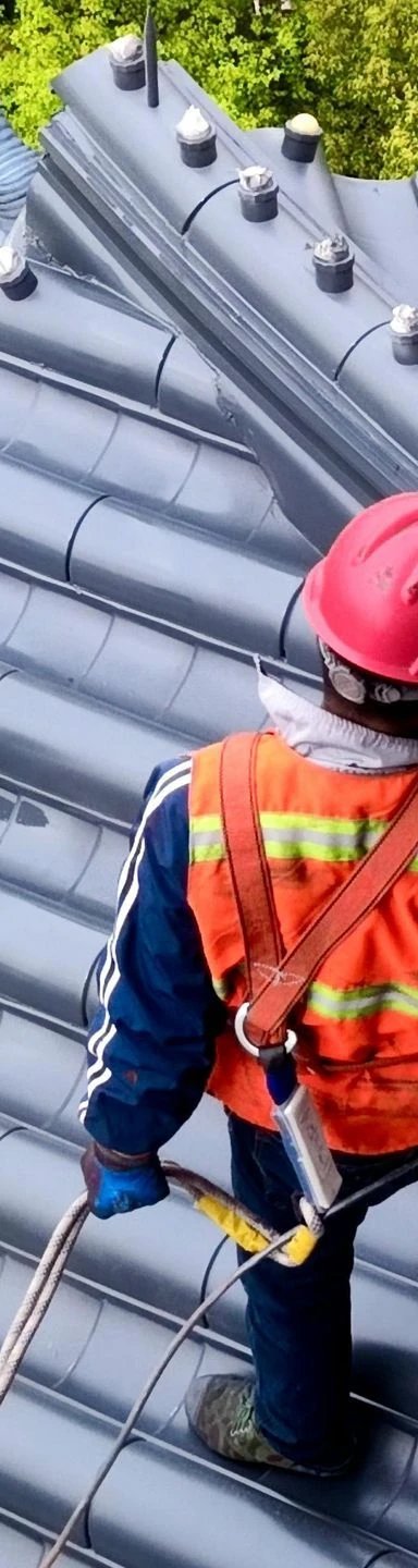 Worker in safety gear on a gray tiled roof.
