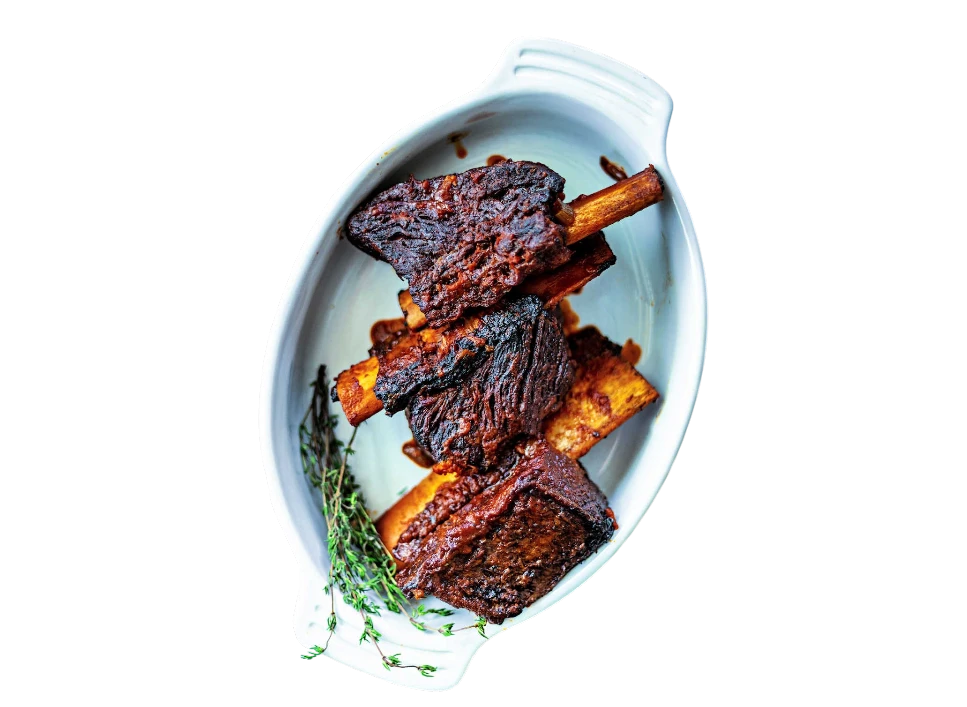 Succulent beef ribs garnished with thyme on a white platter.