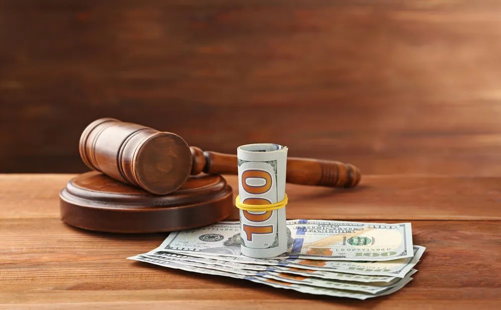 Gavel next to a roll of money and banknotes on wooden surface