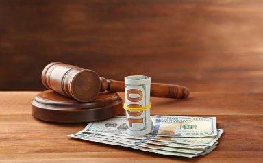 Gavel next to a roll of money and banknotes on wooden surface