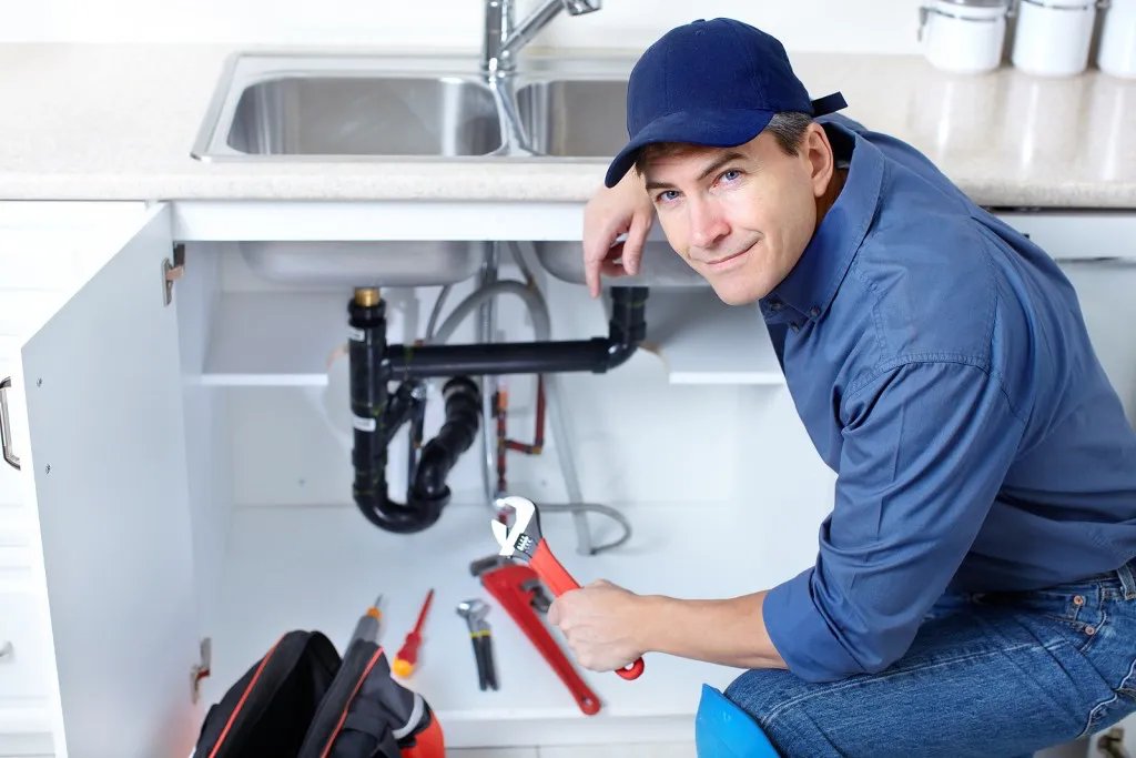 Plumber fixing pipes under a kitchen sink.
