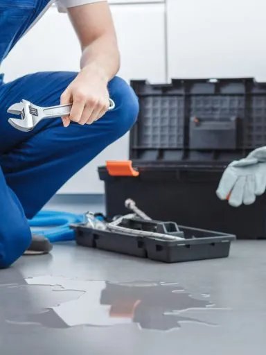 A plumber fixing a leak with a wrench, water on the floor.