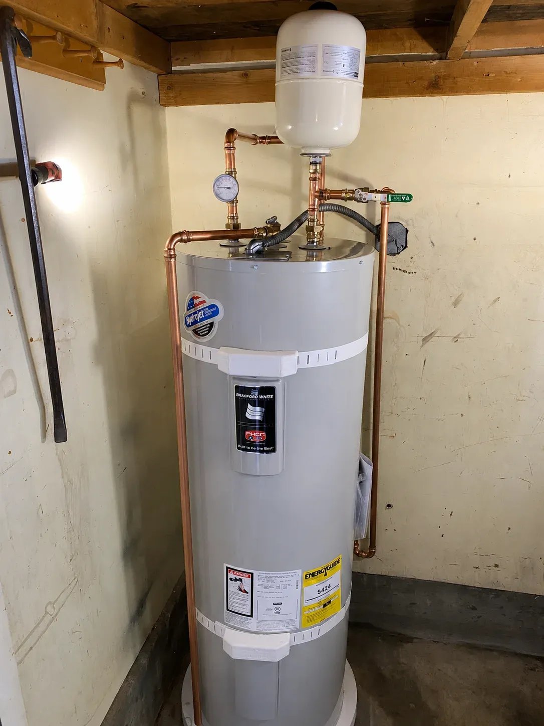 Water heater with copper pipes and gauge in utility room.