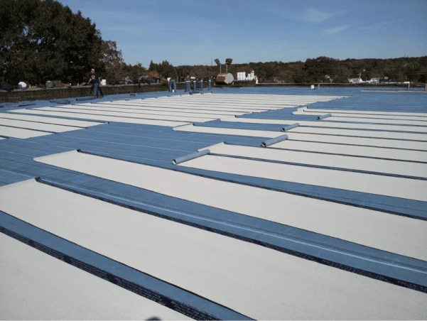 Construction workers laying roofing material on a flat roof.