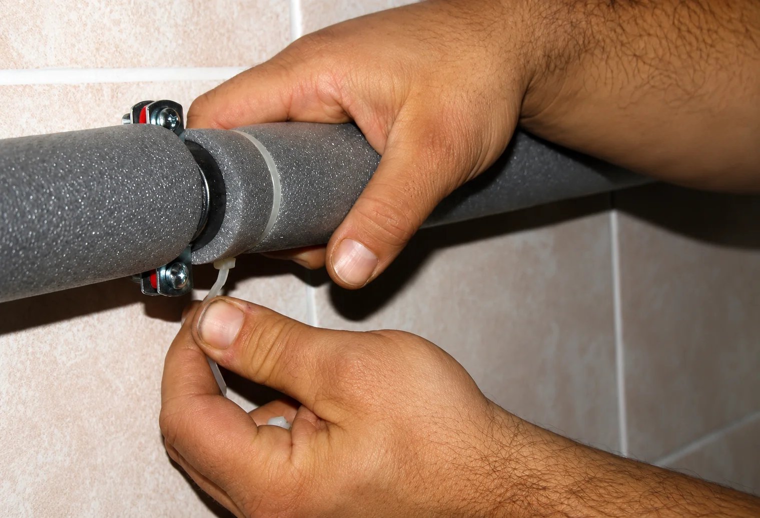 Hands securing a foam-insulated pipe connection