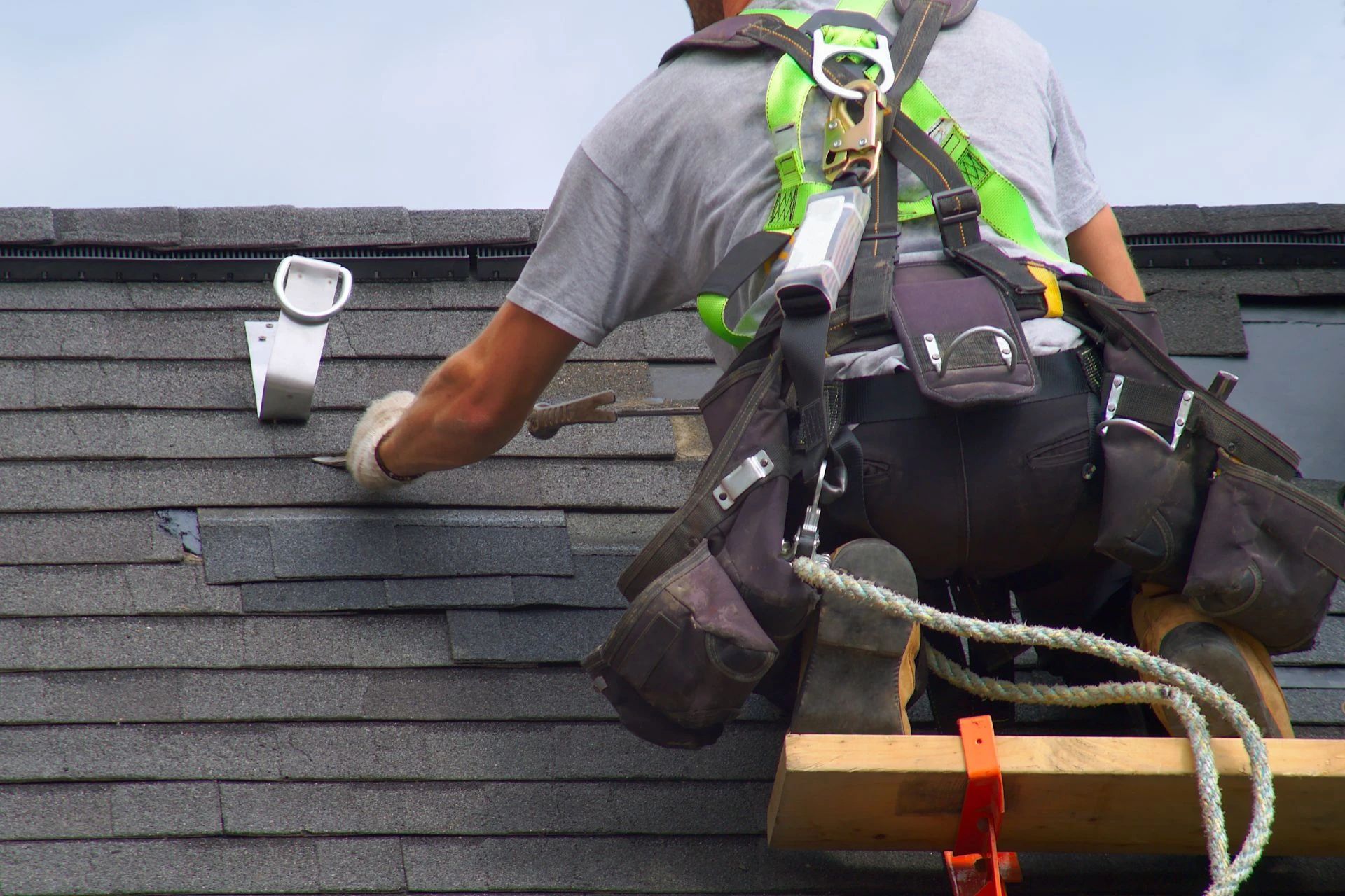 Roofer installing shingles on a roof, wearing a safety harness.