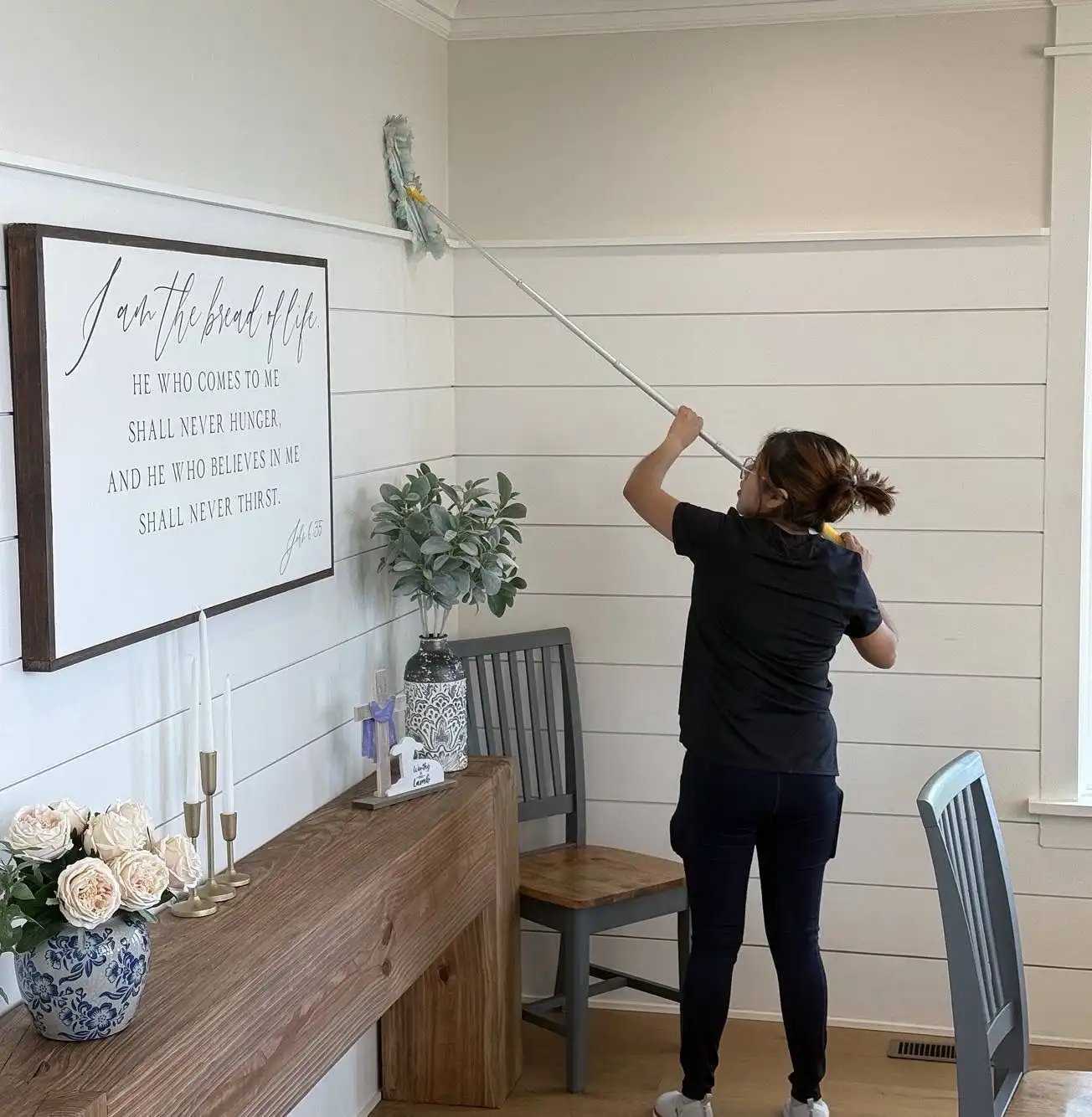 Person cleaning a wall with a mop in a bright room.
