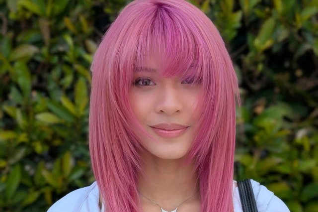 Person with pink hair against green foliage background