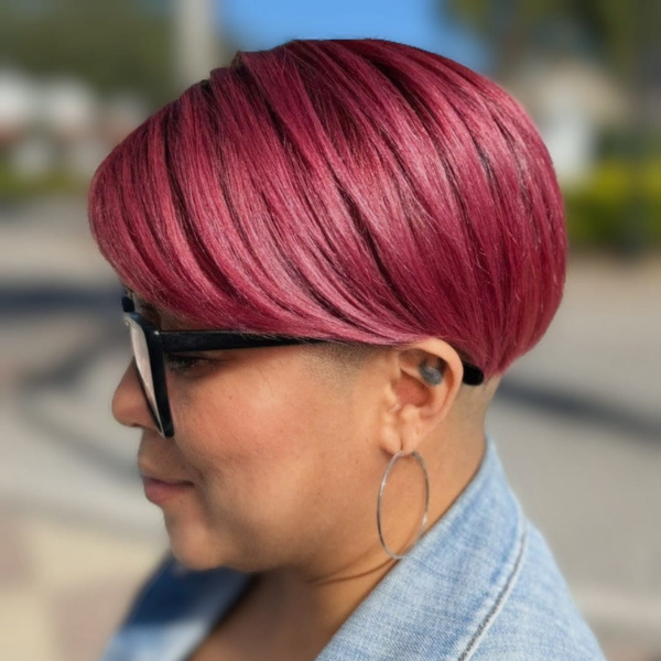 Woman with short pink hairstyle and glasses, smiling.