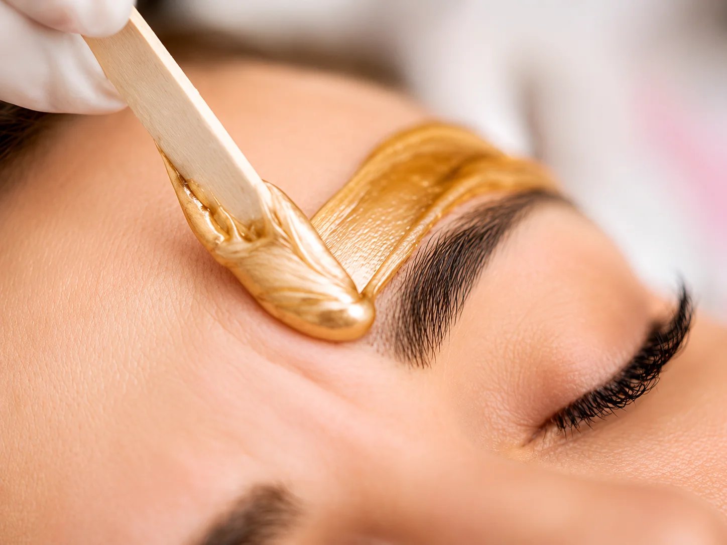 Woman receiving eyebrow waxing with gold wax