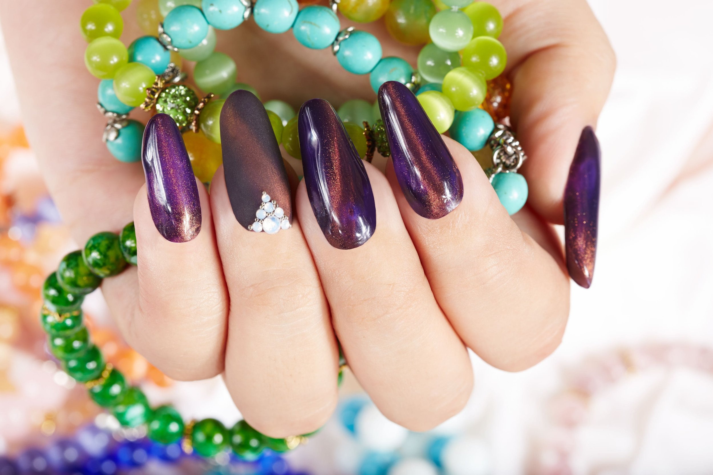 Hand with long purple nails adorned with rings and bracelets.