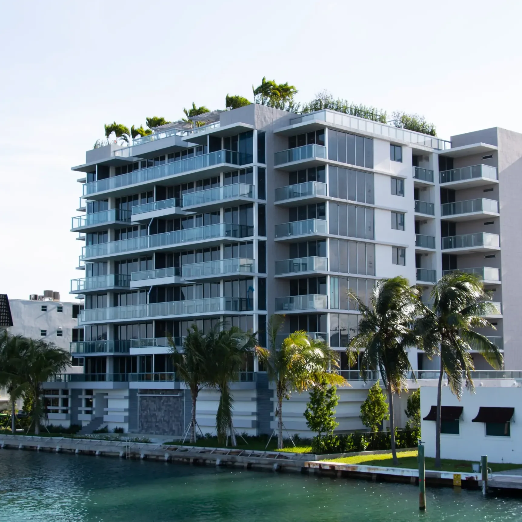 Modern waterfront apartment building with palm trees.