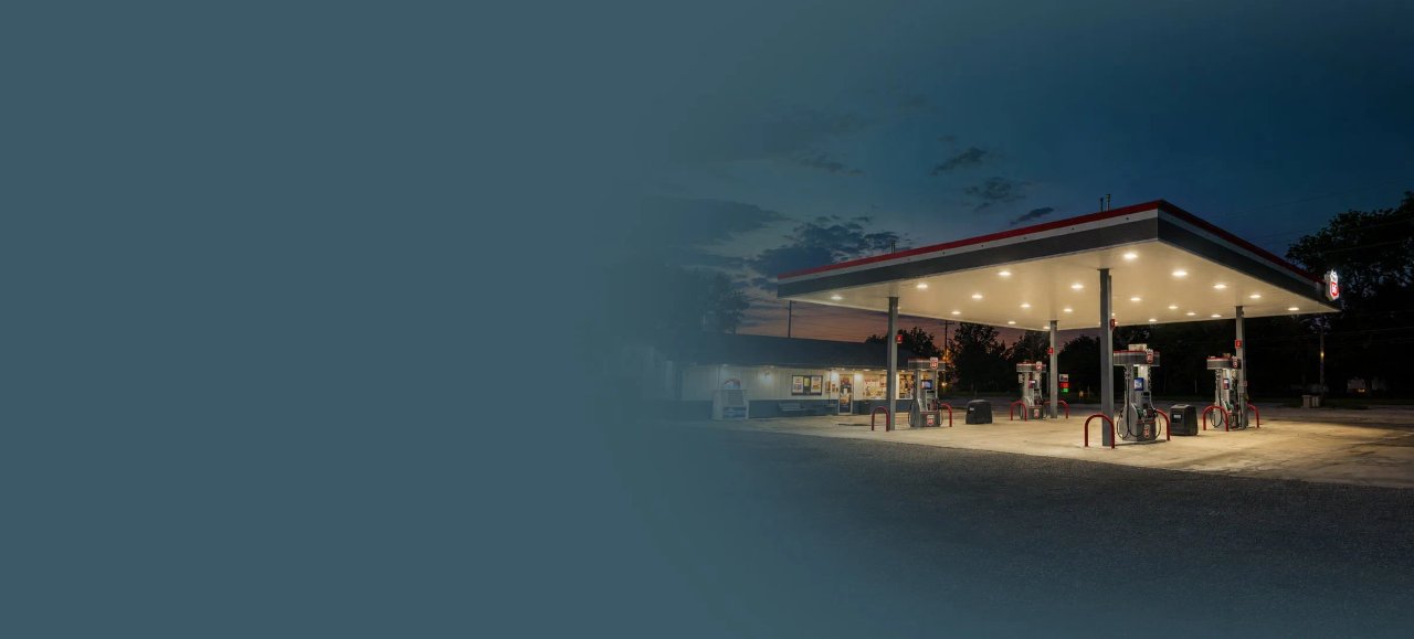A lit gas station at dusk with pumps and a building