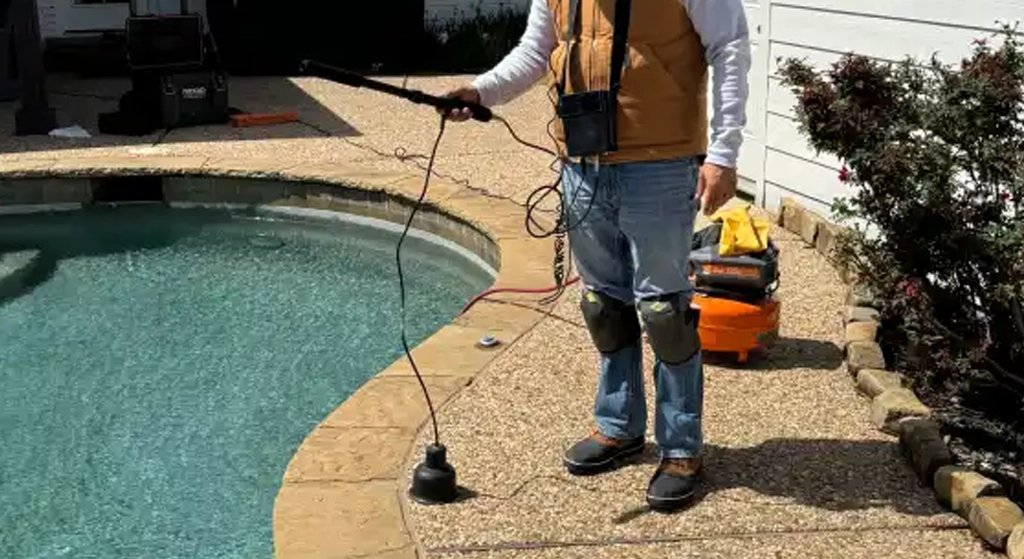 Man using a pool cleaning tool near water.