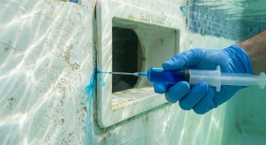 Hand injecting blue liquid into pool skimmer
