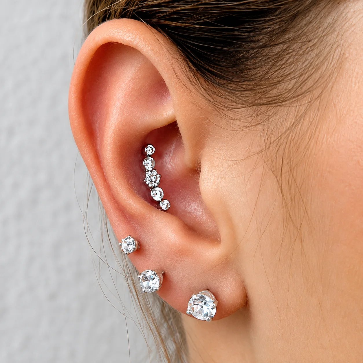 Close-up of a woman's ear adorned with multiple diamond earrings.