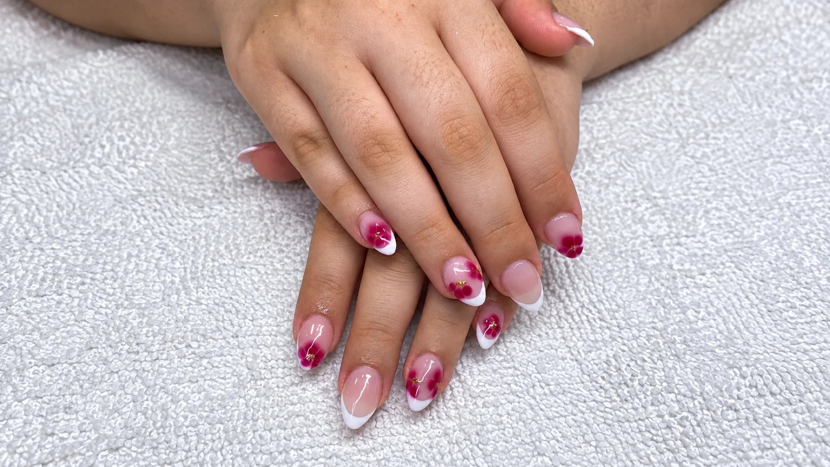Close-up of beautifully manicured nails with pink floral designs resting on a soft white towel.