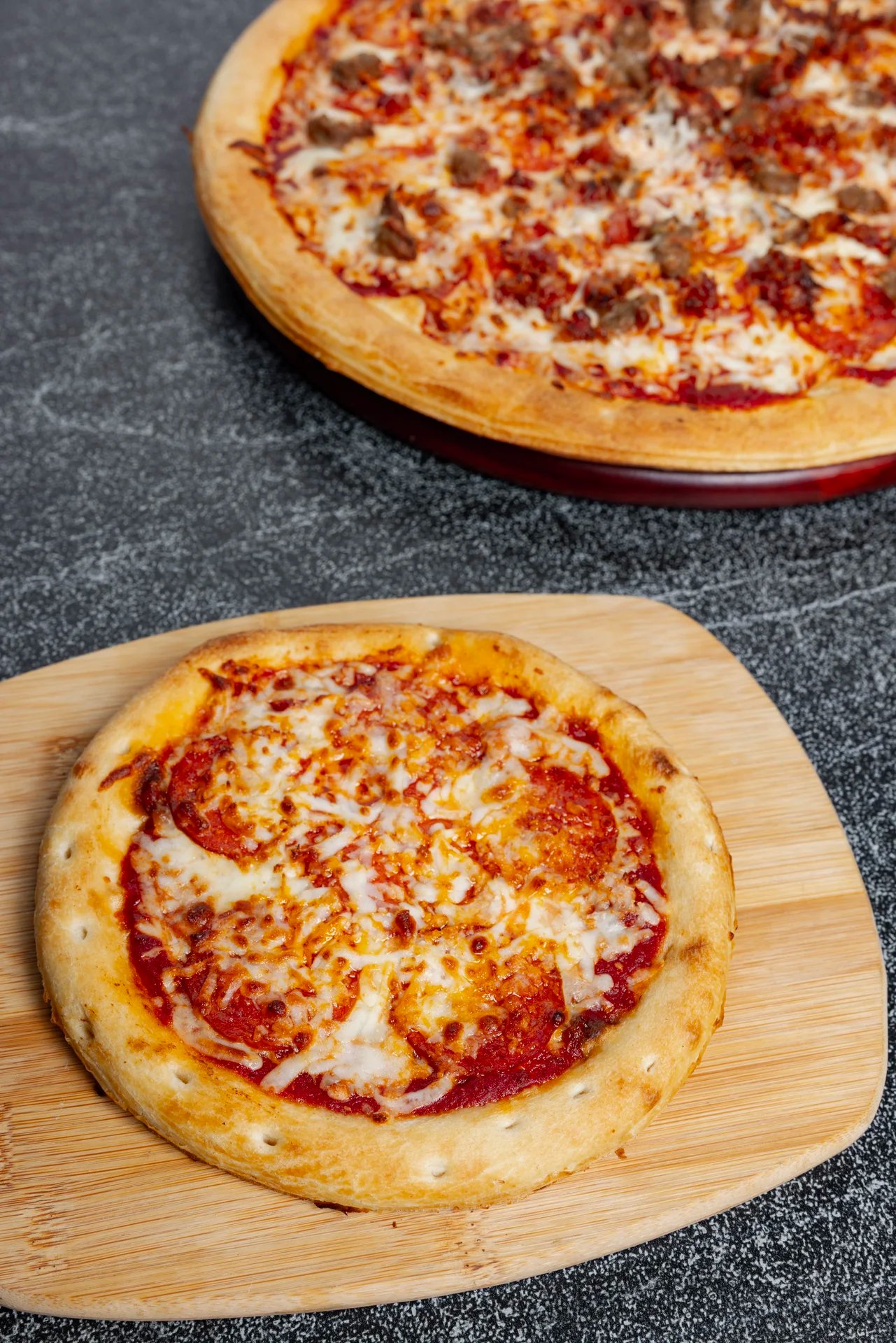 Two pizzas on a wooden board and dark background