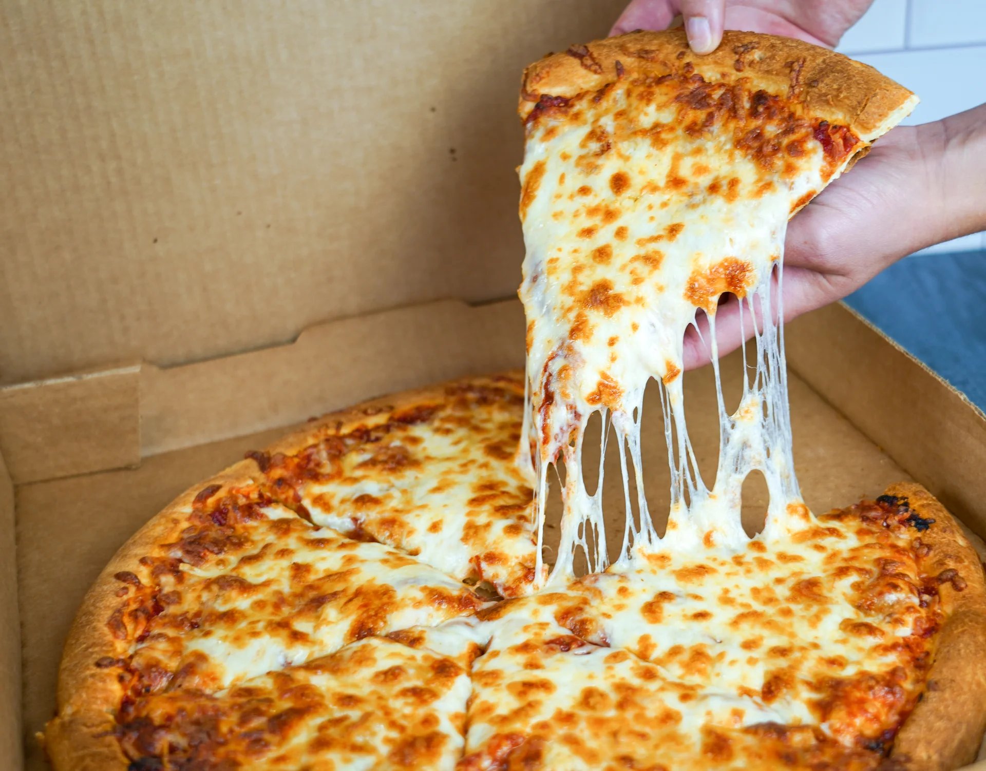 A hand pulling a slice of cheese pizza from an open box.