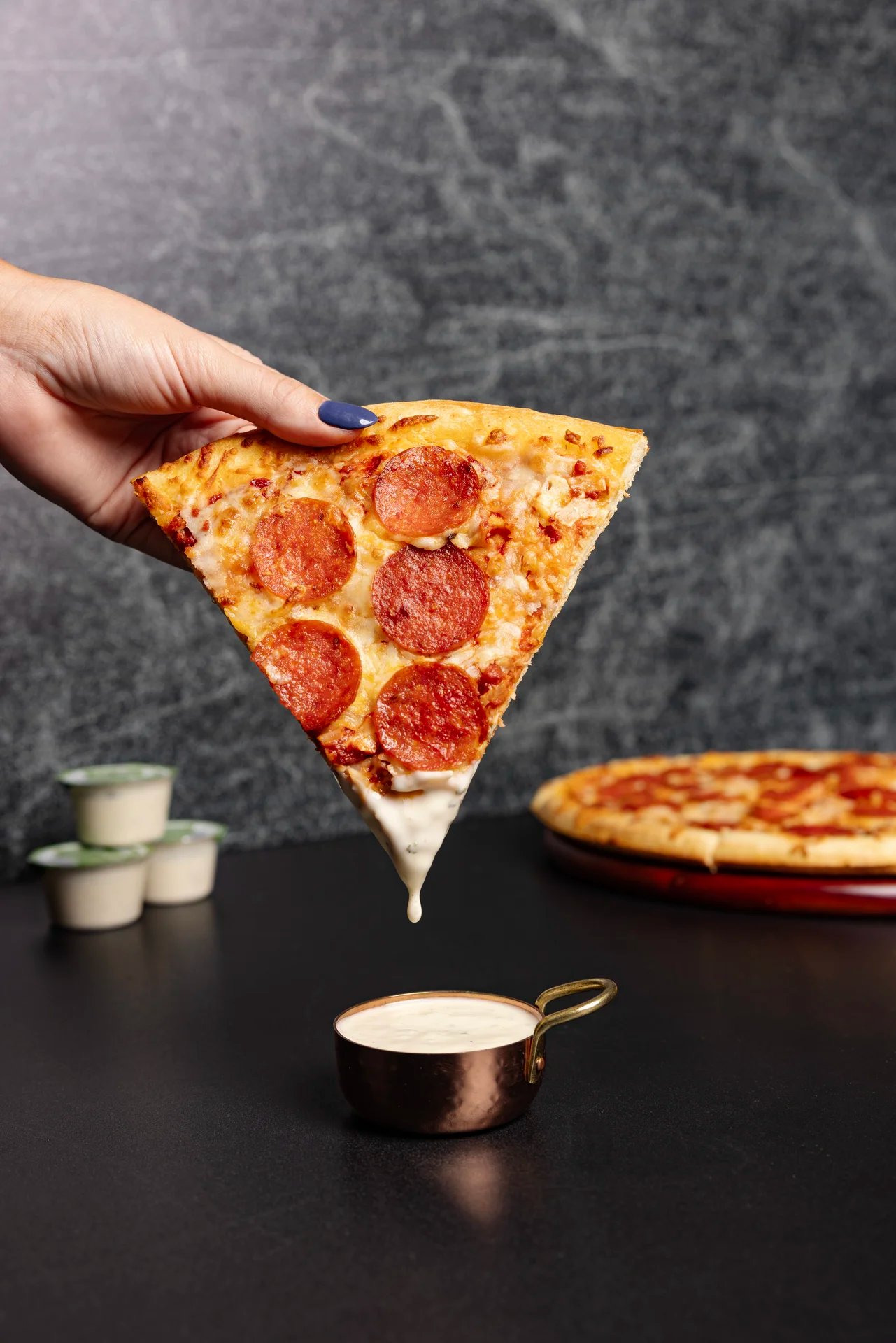 Hand lifting pepperoni pizza slice over dipping sauce