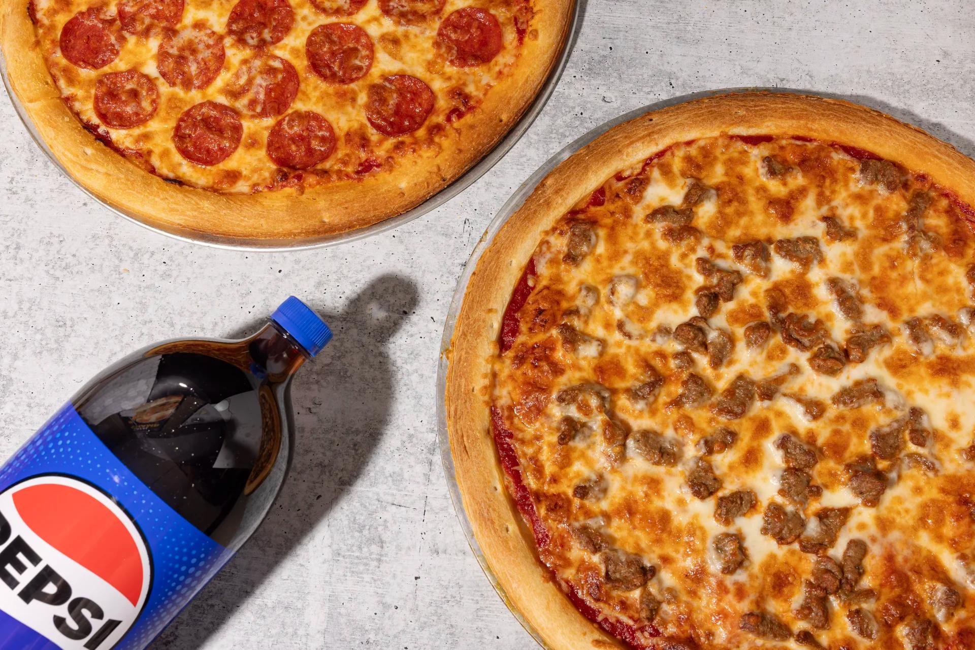 Two pizzas with pepperoni and sausage alongside a bottle of Pepsi.