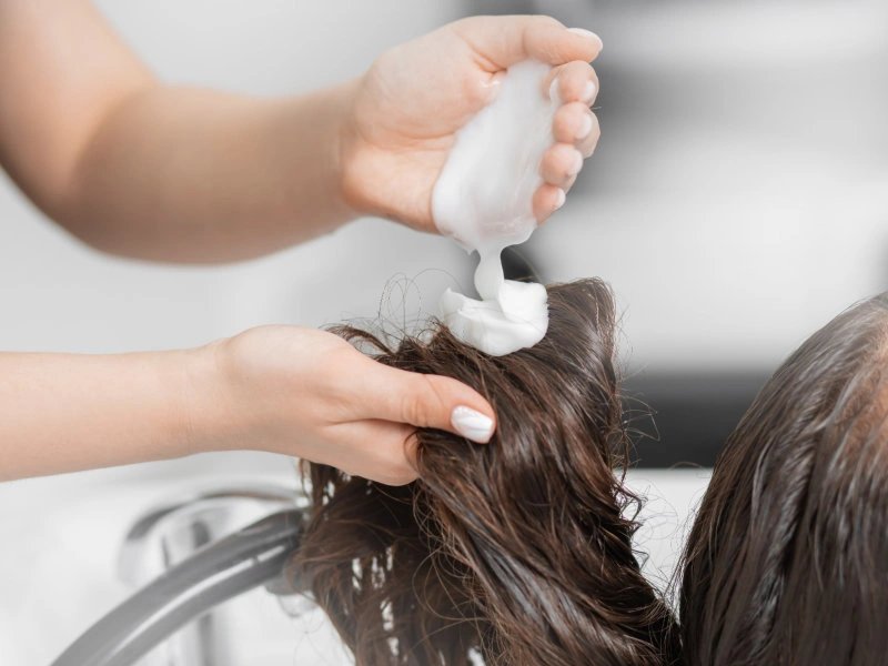 A stylist applying conditioner to hair during a treatment.
