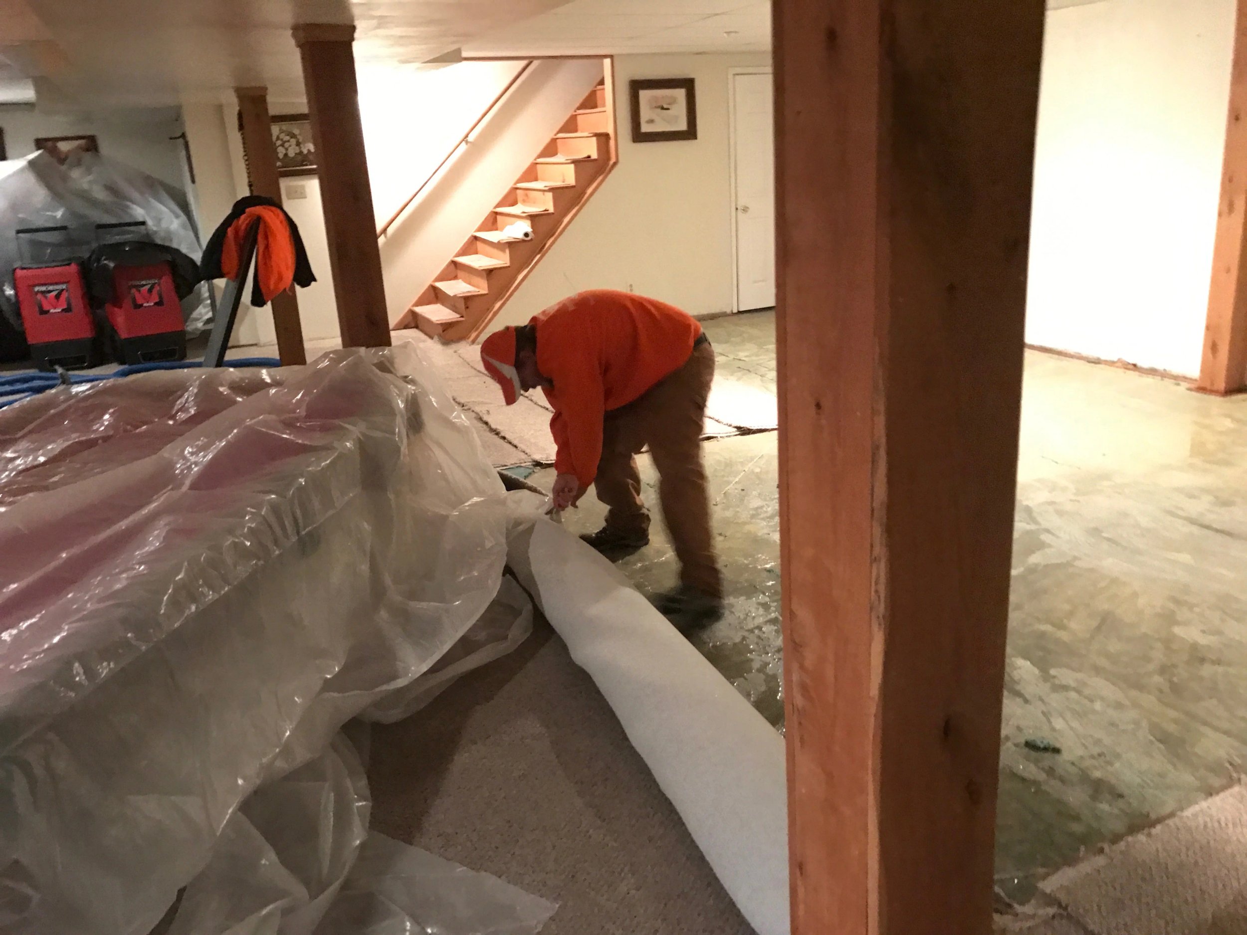 Worker rolling out carpet in basement renovation.
