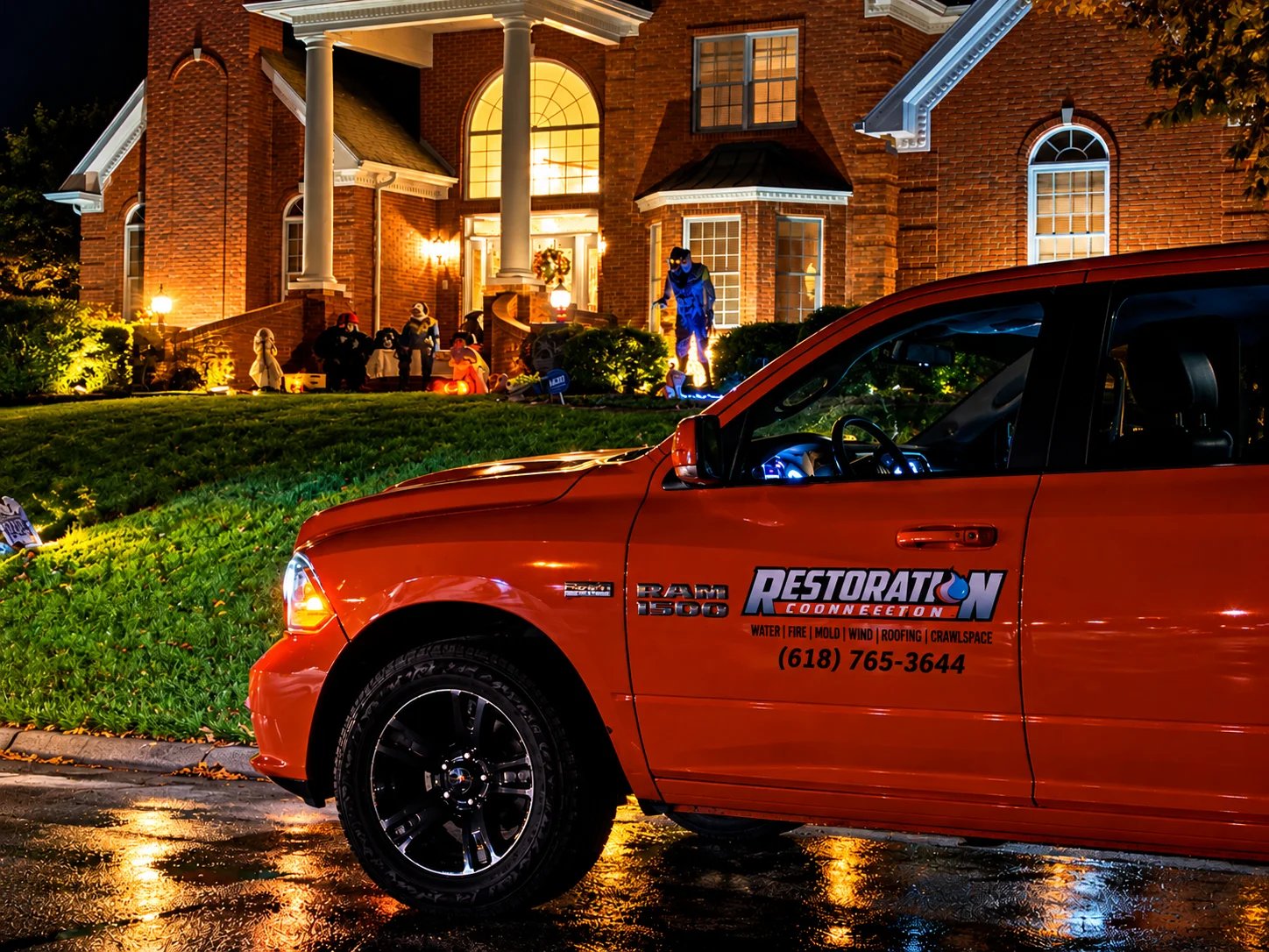 Orange truck parked near a well-lit house decorated for Halloween.