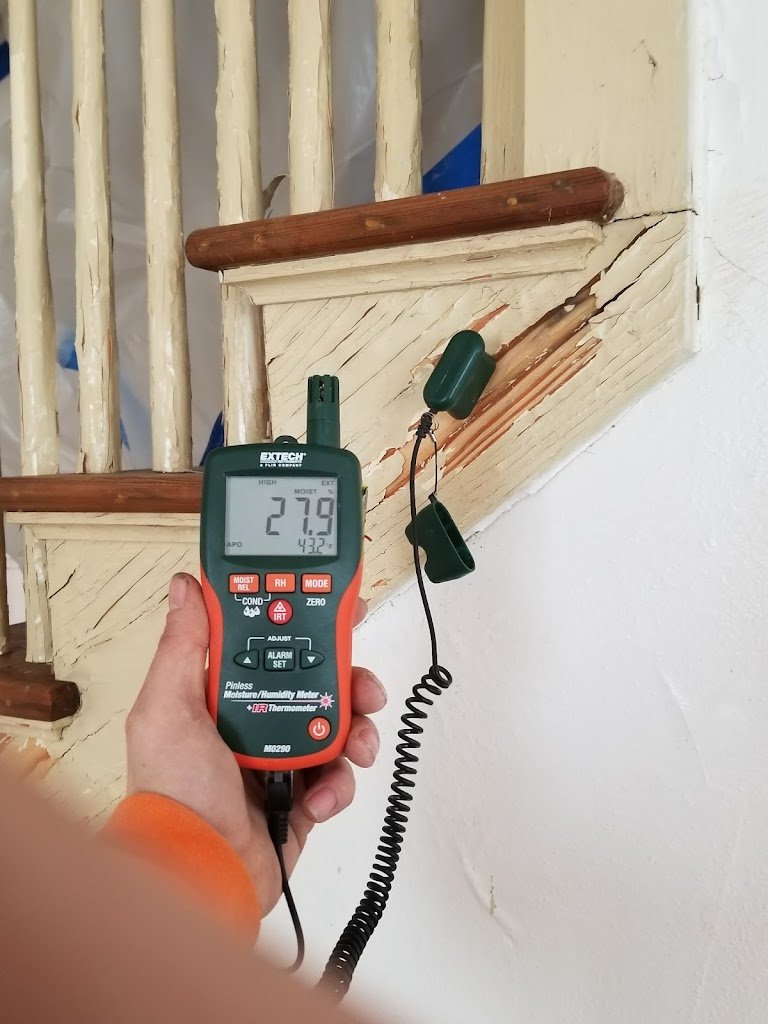 Hand holding a moisture meter near wooden stairs